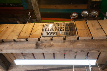 Rusty danger sign fixed to workshop beam. A closeup and low angle view of an old weathered 'danger, keep off' sign attached to a wooden beam inside a garage.