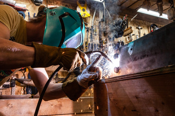 Metalworker operates spot welder indoors. A closeup view of a skilled tradesman operating a metal inert gas welder to join the corners of two steel beams. Process of a metalworker at work.