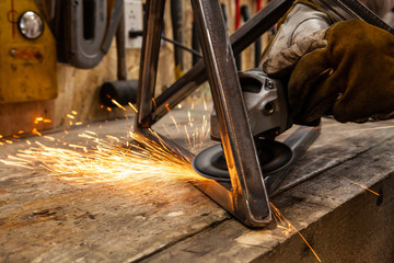 Sparks fly from blacksmith disc grinder. A close up view of an abrasive disc cutter in use. Hands of a skilled worker operate power tool inside a workshop. Hot sparks fly from the abrasive wheel. - Powered by Adobe