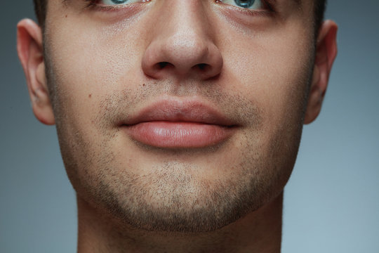 Close-up portrait of young man isolated on grey studio background. Caucasian male model's face and lips. Concept of men's health and beauty, self-care, body and skin care.
