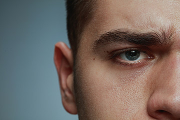 Obraz premium Close-up portrait of young man isolated on grey studio background. Caucasian male model's face and blue eye. Concept of men's health and beauty, self-care, body and skin care, medicine or phycology.