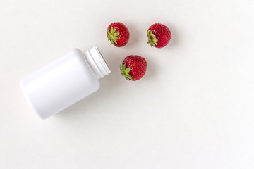 Fresh vitamins as strawberries from medicine white pill bottle on white background.