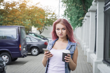 Young hipster woman standing at the street drinking coffee to go and using mobile phone