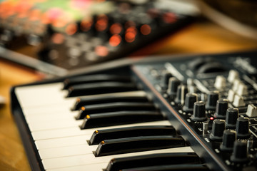 Electronic music production in a home studio. Closeup of an analog synthesizer keyboard, with orange LEDs of a midi controller in the background.
