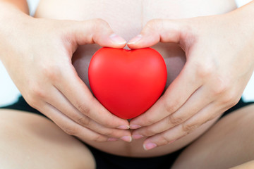 Pregnant woman making a heart with her hands holding red heart on her belly. Heart shape on belly of pregnant woman. Adolescent Pregnancy