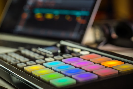 Electronic music production in a home studio. Closeup of coloured LED pads on a midi controller with a blurred laptop screen in the background