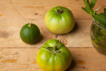 Productos verdes del campo, la hierba de la menta, el tomate verde y la naranja verde sobre una madera rústica.