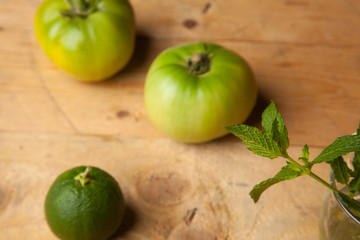 Productos verdes del campo, la hierba de la menta, el tomate verde y la naranja verde sobre una madera rústica.