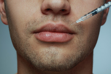 Close-up portrait of young man isolated on grey studio background. Filling botox surgery procedure....