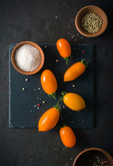 Fresh and juicy orange tomatoes laid out on a dark stone background. View from above. Place for text.