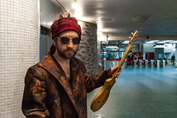 Shaman holds guitar in underground. A bohemian style man looks disheveled as he stands in a tube...