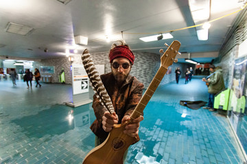 Shaman holds guitar in underground. A wide angled view of a city underground station with blurry...