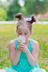 Little beautiful girl sitting on the green grass in the park, soft focus background