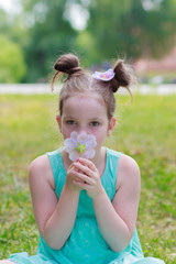 Little beautiful girl sitting on the green grass in the park, soft focus background