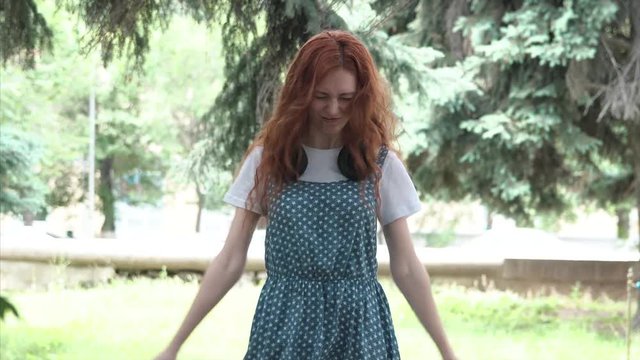 Ginger girl with big headphones in fury. Red-haired girl walks in the park close-up. Young red-headed woman on blurred background of park. Freckled teenager outdoor. 