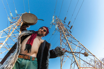 Sacred man beneath electricity towers. A young Caucasian shaman is viewed from below as he stands...