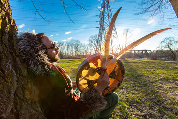 Shaman meditates under tree in park. A close up and side profile view of a medicine man meditating beneath a mature tree at sundown, he looks calm and relaxed as he holds sacred objects in hand.
