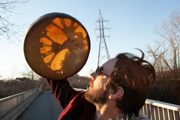 Spiritual man holds sacred drum to sun. A closeup and side profile view of a shaman as he raises a...