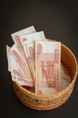 A lot of banknotes worth five thousand rubles are in a round wooden wicker box.