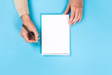 Woman's hands with perfect manicure holding pencil and  notepad as mockup for your design. blue background, flat lay style.