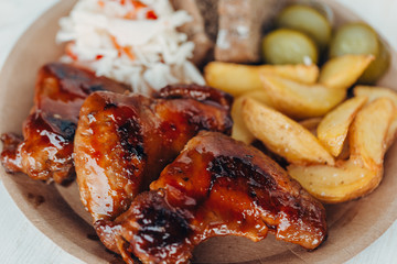 Delicious fried chicken wings with sauce, fried potatoes, cucumber, cabbage and khlobe in a paper plate on a wooden table. takeaway street food