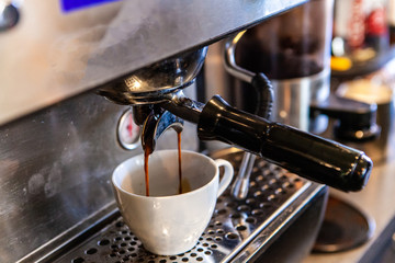 Filtered espresso coffee machine. Aromatic coffee is viewed closeup, as it filters from a machine inside a coffeehouse, slowly drips into a white ceramic cup.