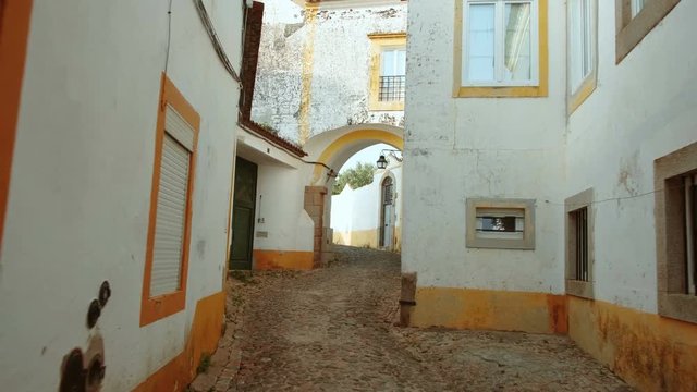 Walking along the narrow and picturesque streets of Evora, Portugal, featuring the famous whitewashed houses with yellow accents. Enclosed by medieval walls, Evora is a UNESCO World Heritage