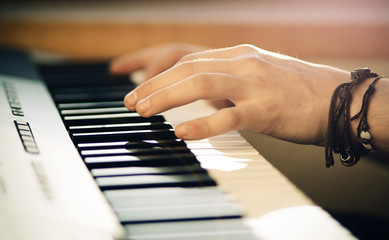 Fototapeta premium A man with a brown bracelet on his hand plays a beautiful arrangement of the melody on the synthesizer on a Sunny bright day.