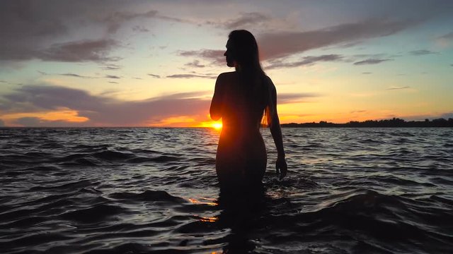 Silhouette of young, long hair woman with slim body in the sea. Sunset time. 