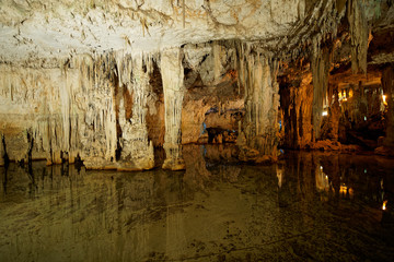 Imposing stalactites and stalacmites reflecting in a small underground lake inside the limestone cave (Tropfsteinhöhle) Grotta di Nettuno in Sardegna (Italy)
