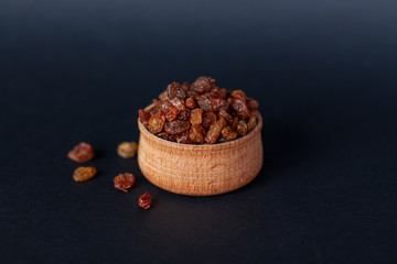 Close-up of handful of brown raisins on a wooden plate in warm tones. Eastern sweets. Healthy snack. Dried grapes
