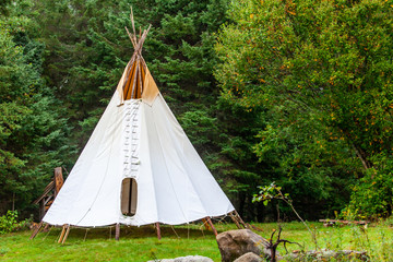 Fusion of cultural & modern music event. A rustic tipi tent is viewed by woodland, similar to that...