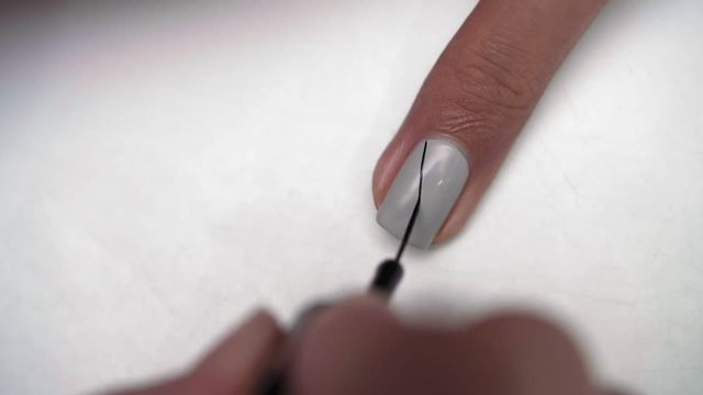 Close up of female hand applying black stripes over polished female fingernail using thin brush