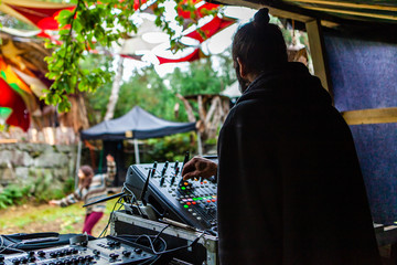 Fusion of cultural & modern music event. An over the shoulder view of bohemian DJ using electronic music equipment to entertain people during a music festival celebrating a mix of modern & old sounds