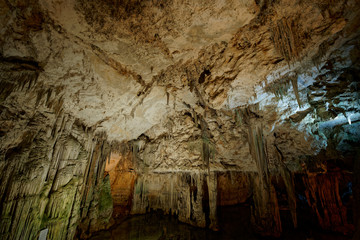 Fototapeta na wymiar Imposing stalactites and stalacmites reflecting in a small underground lake inside the limestone cave (Tropfsteinhöhle) Grotta di Nettuno in Sardegna (Italy) 