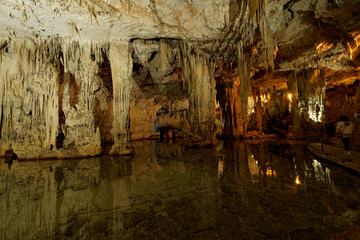 Imposing stalactites and stalacmites reflecting in a small underground lake inside the limestone cave (Tropfsteinhöhle) Grotta di Nettuno in Sardegna (Italy)  © Adrian