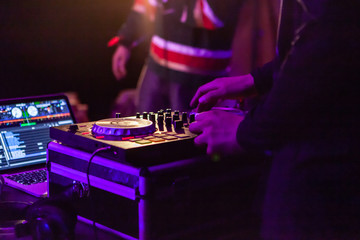 Fusion of cultural & modern music event. A closeup view on the hands of a DJ as he uses an electronic turntable attached to a laptop during a music festival, viewed from behind by night.