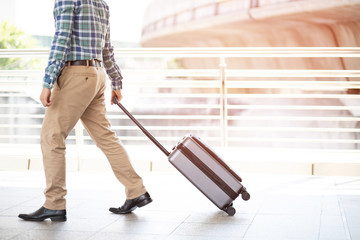 businessman walking outside public transport building with luggage in rush hour. Business traveler pulling suitcase in modern airport terminal. baggage business Trip.  Copy space. soft focus.