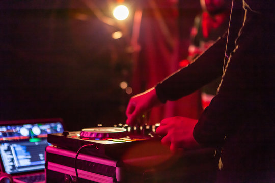 Fusion of cultural & modern music event. Hands of a modern electronic deejay are seen up close, as he operates mixing equipment at a music concert by night artificial lighting is blurred in background