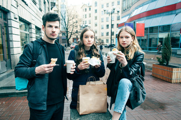 lifestyle and people concept: two girls and guy eating fast food on city street together having fun, drinking coffee