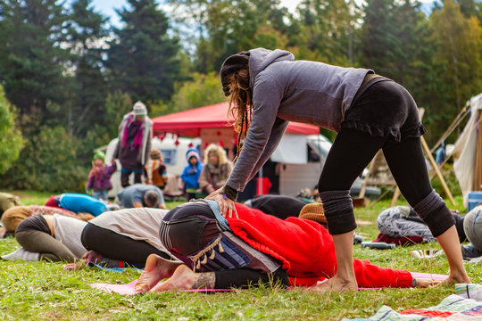 Fusion of cultural & modern music event. People are seen relaxing and stretching in a festival campsite, as a bohemian styled person performs lumbar back massage on one person.