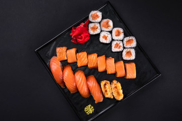 Top view close up of sashimi sushi set with chopsticks and soy on black background. Korea rolls and green tea cups and teapot, copy space. Japanese food.