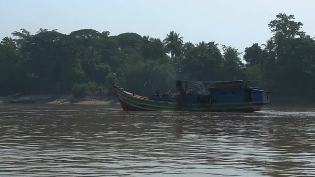 A daylight steady shot from inside a moving motorboat traveling in the murky river and passing by an old pump boat carrying some passengers.