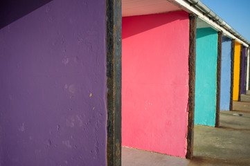 A row of concrete beach hut porches have been painted in different colours and lead into the distance - Image
