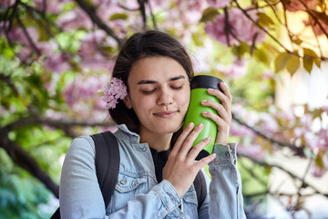 Young smiling woman hold green bottle on the background of blooming sakura