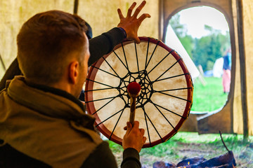 Fusion of cultural & modern music event. An over the shoulder view of a spiritual man playing native drum as he sits inside a teepee tent during a celebration of Native American culture, room for copy