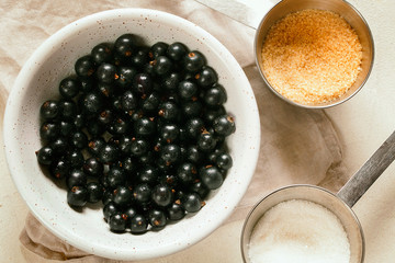Ripe and tasty freshly harvested organic black currant with water drops and sugar in white ceramic bowl close-up top view.Homemade preserved fruit or berries preparation.Healthy vegan snack