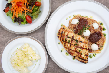 Grilled chicken, cheese and tomato rice, carrot, letucce and sliced pineapple on dishes over wooden table