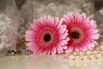 Festive background with pink flowers, pearl necklace and wedding rings