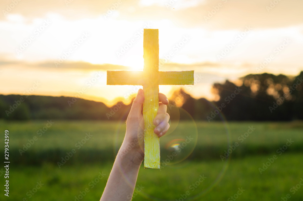 Wall mural teenager girl holding a the cross in hand during beautiful sunset. hands folded in prayer concept fo